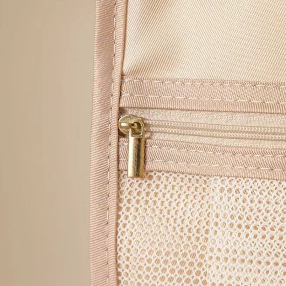 Beige travel pouch with gold zipper and visible brand logo on a beige background