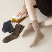Person wearing Camel Heather socks with a set of three pairs of socks on a light surface.
