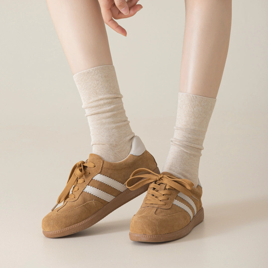 Brown sneakers with white stripes worn with Oatmeal Heahter socks on a neutral background