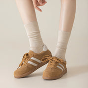 Brown sneakers with white stripes worn with Oatmeal Heahter socks on a neutral background